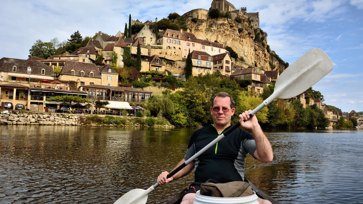 A canoeist on the Dordogne River, facing the village and the castle of Beynac.
