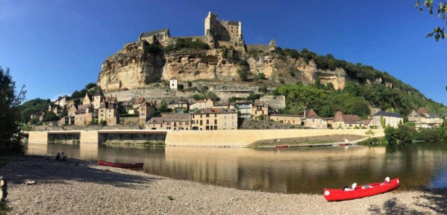 Canoes on the banks of the Dordogne River, with the village and castle of Beynac in the background