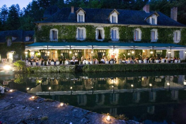 The illuminated facade of the Manoir d’Hautegente and its reflection in the water